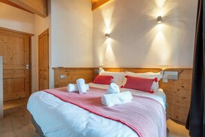 Una cama bien tendida con ropa de cama blanca y roja, un cabecero de madera y dos lámparas fijadas a la pared.