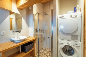 A modern bathroom with a glass-enclosed shower, a sink, a wooden vanity, and a stacked washer and dryer.