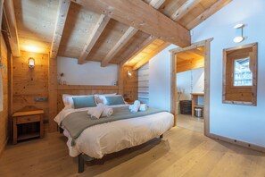 Une chambre aux murs lambrissés, avec un lit, des tables de chevet et une vue sur l’extérieur grâce à une porte ouverte.