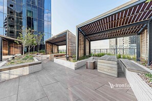 A rooftop garden with wooden benches, planters, and a pergola structure. - Luxury Marina Tower Stay | Waterfront & City Views (Docklands)