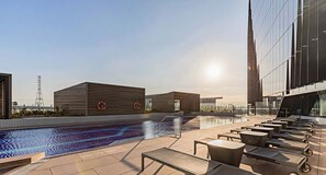 Un espace piscine sur le toit, avec des chaises longues et un bâtiment moderne en arrière-plan.
