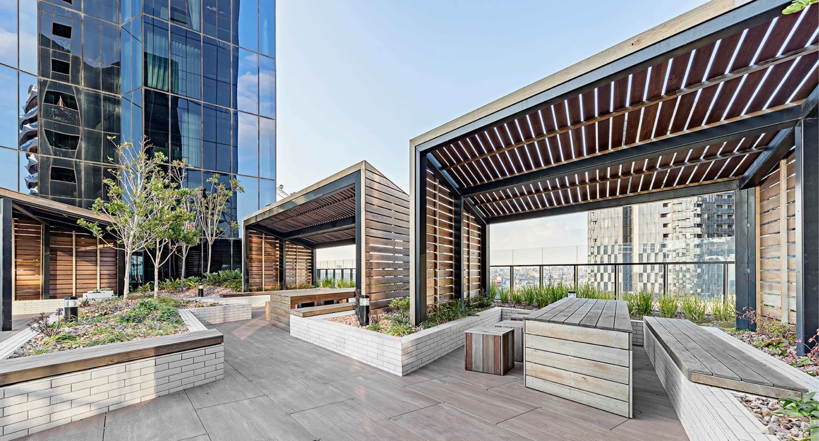 A rooftop garden with wooden benches, planters, and a pergola structure.