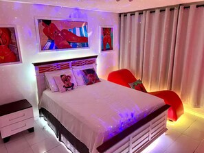 Ein Schlafzimmer mit einem Bett, einem Nachttisch, einem roten Sessel und Bildern an den Wänden.