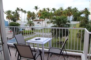 A balcony with two chairs and a small table, overlooking a pool and palm trees.