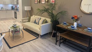 Un salon moderne comprenant un canapé, une table basse, une table à manger et des chaises. Il y a également un coin cuisine avec des placards et un réfrigérateur.