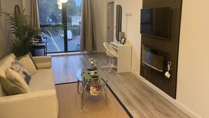 Un salon moderne avec un canapé, une table basse en verre, un téléviseur fixé au mur et une vue sur la rue.