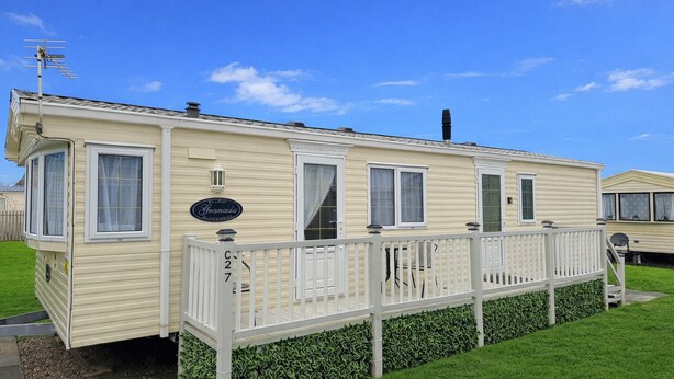A mobile home with a fenced deck, a sign reading 'Granada,' and a number 'C27' on the gate.