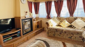 A living room with a television, fireplace, sofa, and windows with curtains.