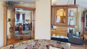 A living room with a glass coffee table, a patterned sofa, and a wooden cabinet with glass shelves.