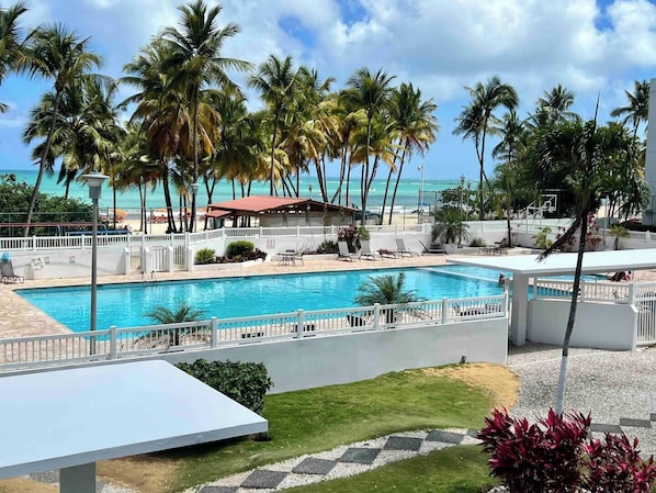 Un área de piscina con sillones de descanso, palmeras y vistas al océano.