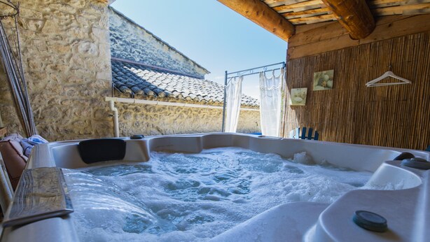 Een hottub met een achtergrond van een stenen muur, een houten plafond en een betegeld dak.