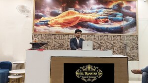A hotel reception desk with a large painting of deities in the background, a modern reception area, and a logo for Hotel Ramayan Inn. - Hotel Ramayan inn (Rishikesh)