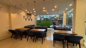 A restaurant with a modern interior, featuring wooden tables and chairs, pendant lighting, and a view of the outdoors through large windows. - Hotel Ramayan inn (Rishikesh)
