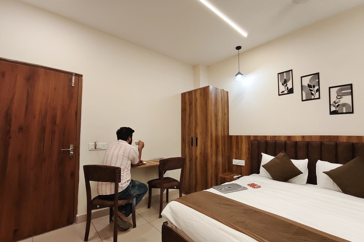 Un dormitorio con una cama, un escritorio y una silla. Hay un armario de madera, una mesita de noche y una lámpara de pared.