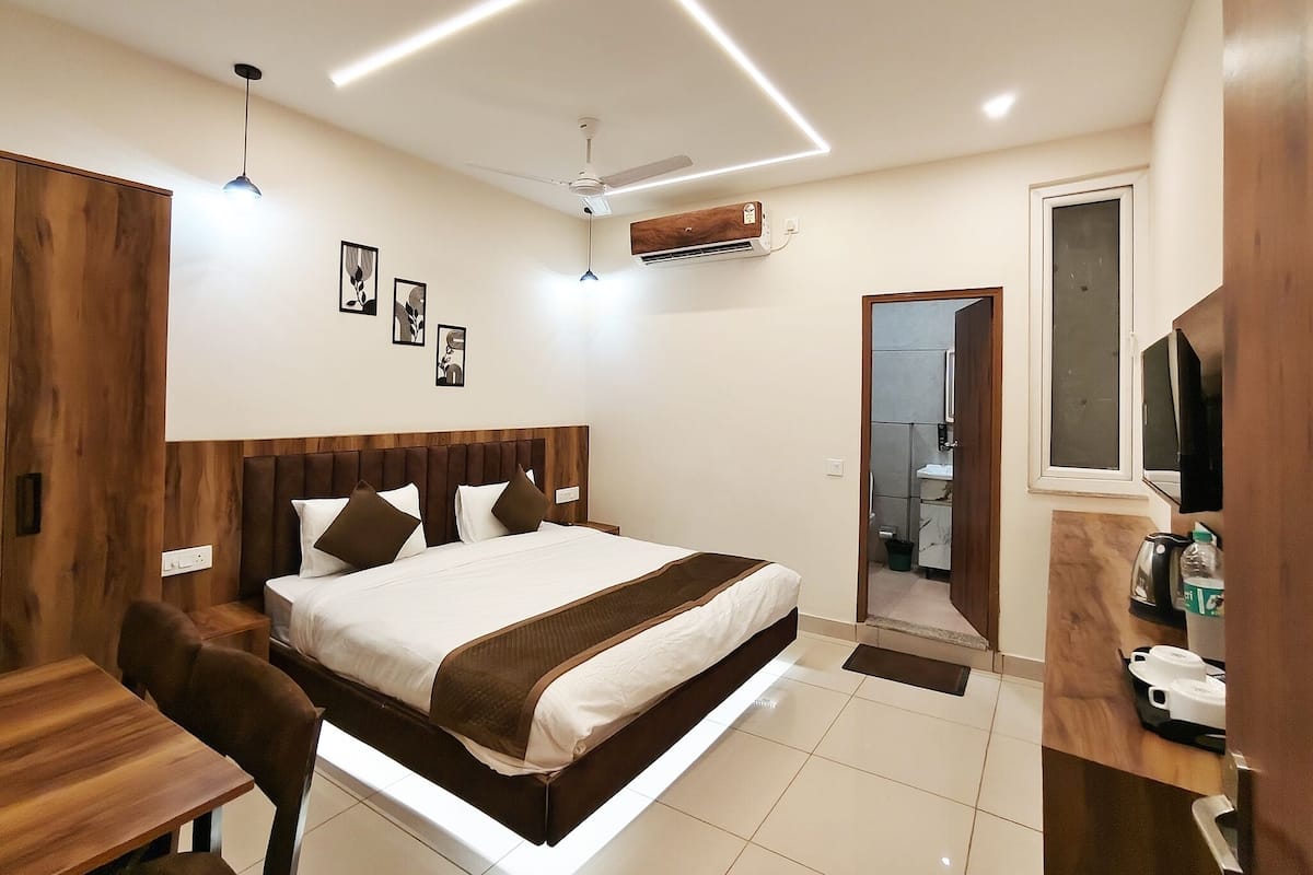 A modern bedroom with a bed, bedside table, and a desk. There is a ceiling fan, an air conditioning unit, and a TV mounted on the wall.