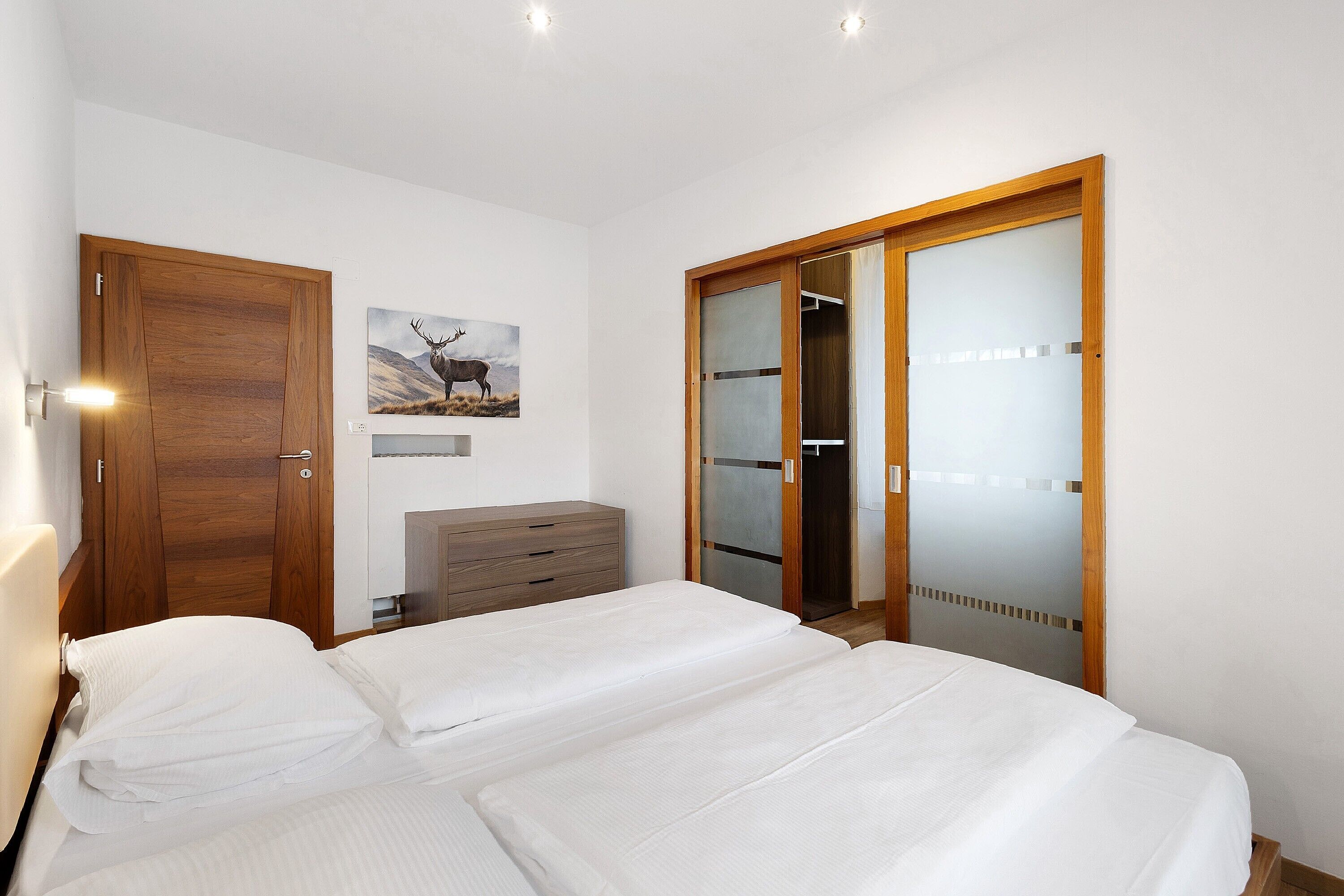 Een slaapkamer met een bed, een houten garderobe, een dressoir en een inloopkast met glazen schuifdeuren.
