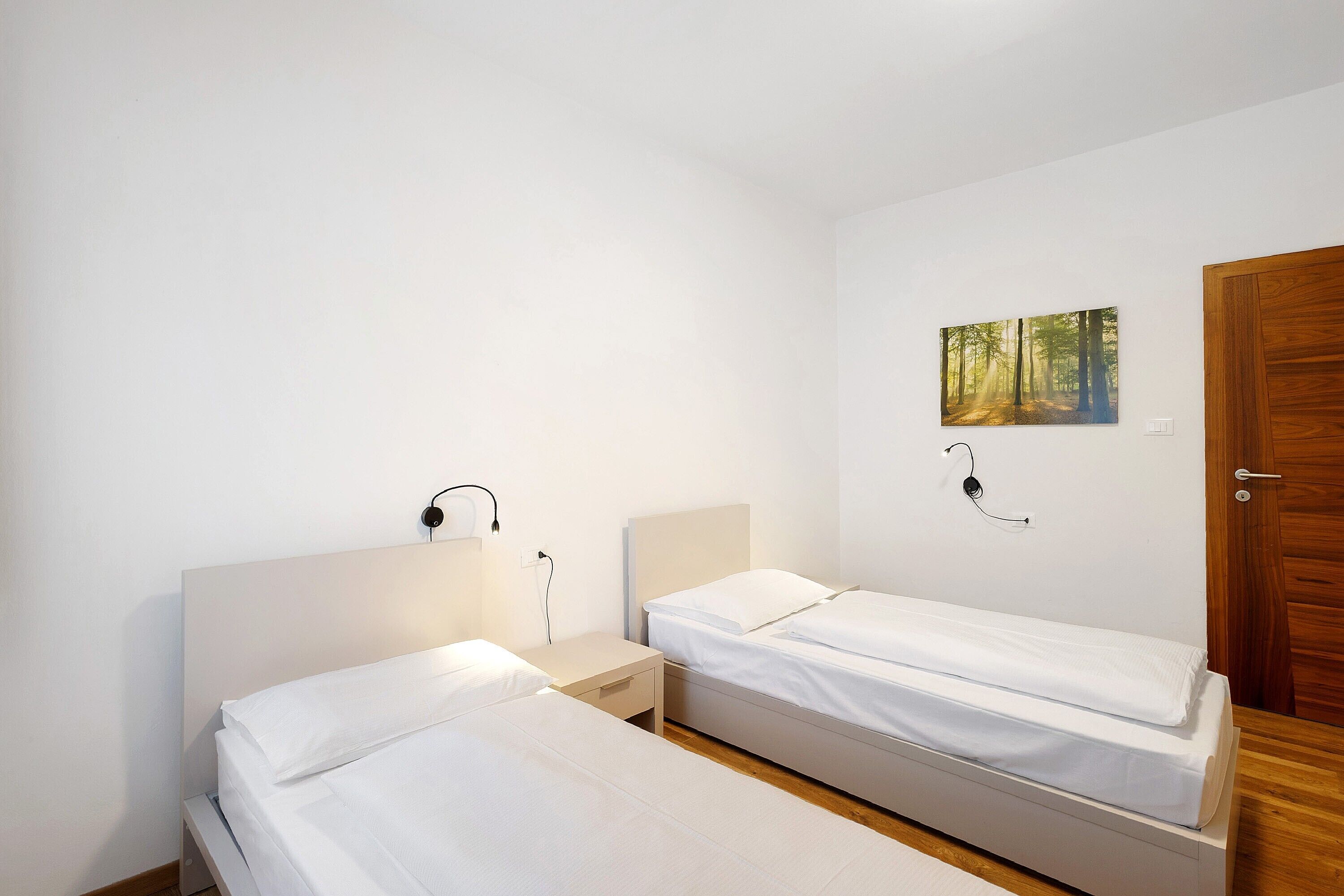 A bedroom with two single beds, a nightstand, a wall-mounted lamp, and a door.