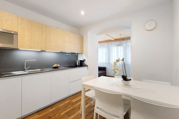 Une cuisine moderne avec des meubles en bois, un plan de travail blanc et un coin repas comprenant une table et des chaises blanches.
