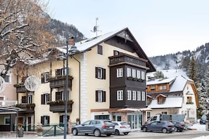 A multi-story building with balconies, a visible entrance, and a snow-covered mountain in the background.