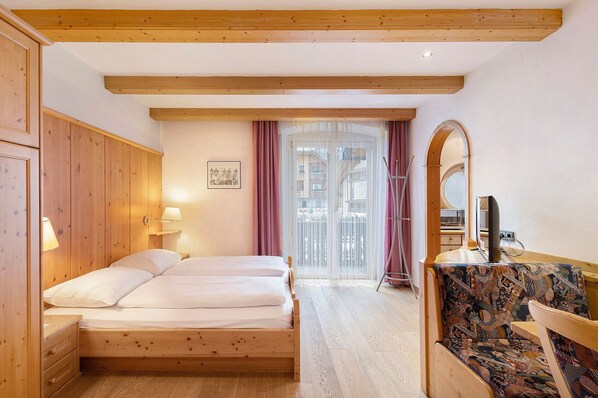 A room with a wooden bed, a chair, a desk with a computer, and a window with curtains.