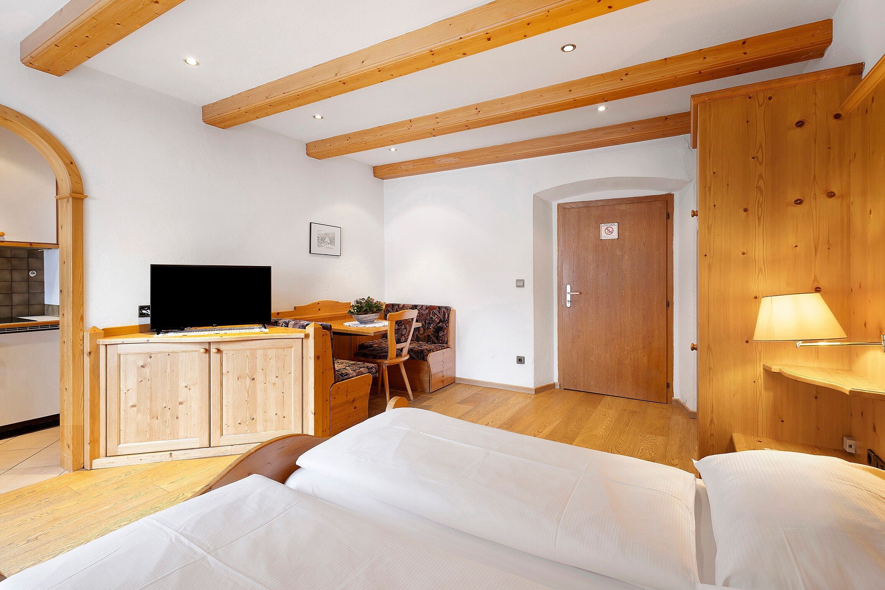 Una camera da letto con un letto, travi a vista in legno, una TV, una scrivania con una sedia e una porta.