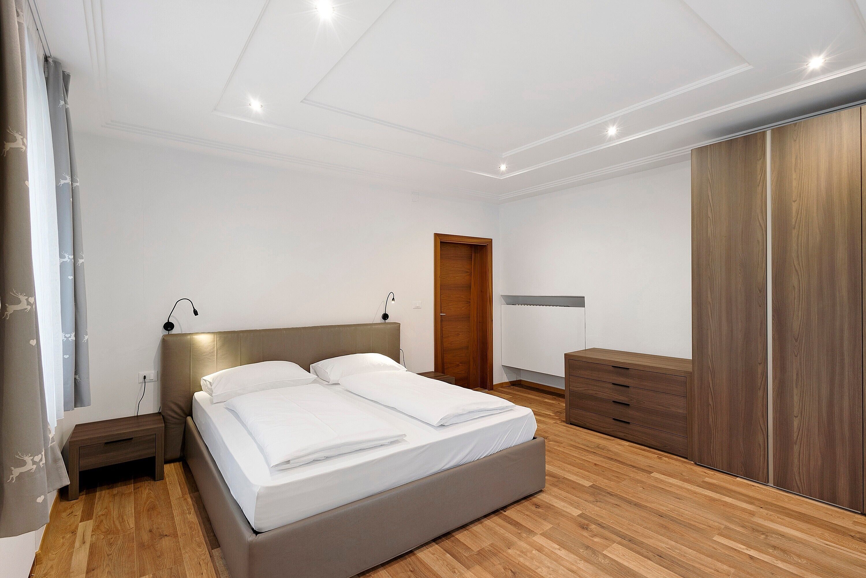 Een slaapkamer met een bed, nachtkastjes, een kledingkast en een nachttafeltje.