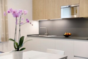 A modern kitchen with a stainless steel oven, a sink, and a bowl of fruit on the counter.