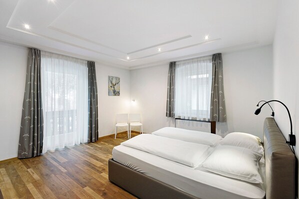 A bedroom with a bed, two chairs, a lamp, and a painting on the wall.