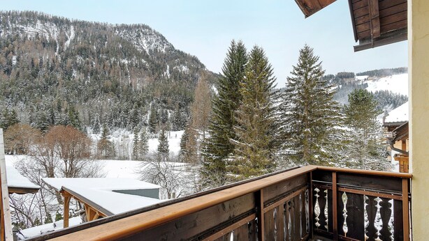 Un balcon en bois offrant une vue sur des montagnes et des arbres couverts de neige.