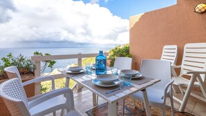 Een tafel gedekt met borden, glazen en een waterfles op een balkon met uitzicht op zee.