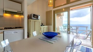 Een keuken met een vaatwasser, magnetron en een eethoek met een tafel, stoelen en een blauwe kom.