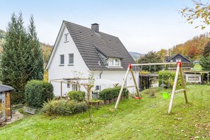 Ein Haus mit geneigtem Dach, einem eingezäunten Garten und einer Schaukel.