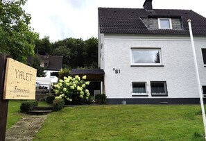 Ein weißes Gebäude mit schwarzem Dach, einer Schautafel und einem Garten mit Hortensien.