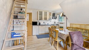 Una cocina compacta con armarios de madera, una mesa de comedor con sillas, una escalera y un pequeño rincón de descanso con un banco.