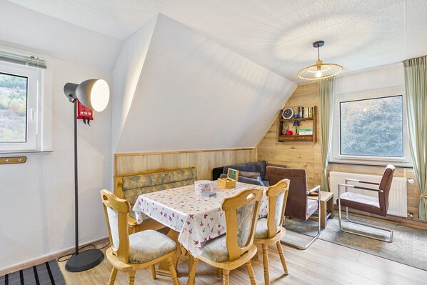A dining area with a table set for four, wooden chairs, a floor lamp, and a bookshelf with books and a clock.
