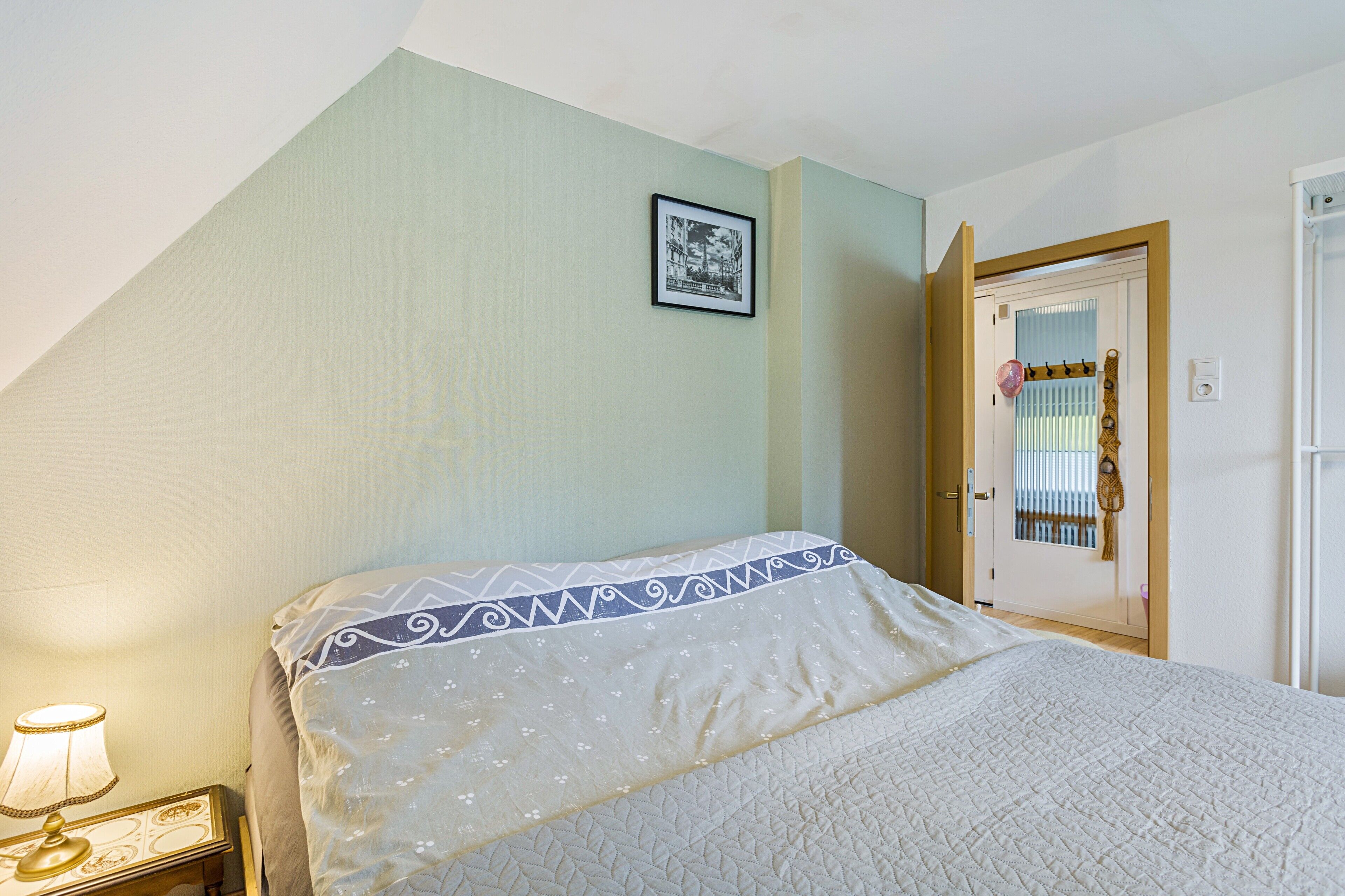 A bedroom with a bed, a nightstand with a lamp, a door with a mirror, and a framed picture on the wall.