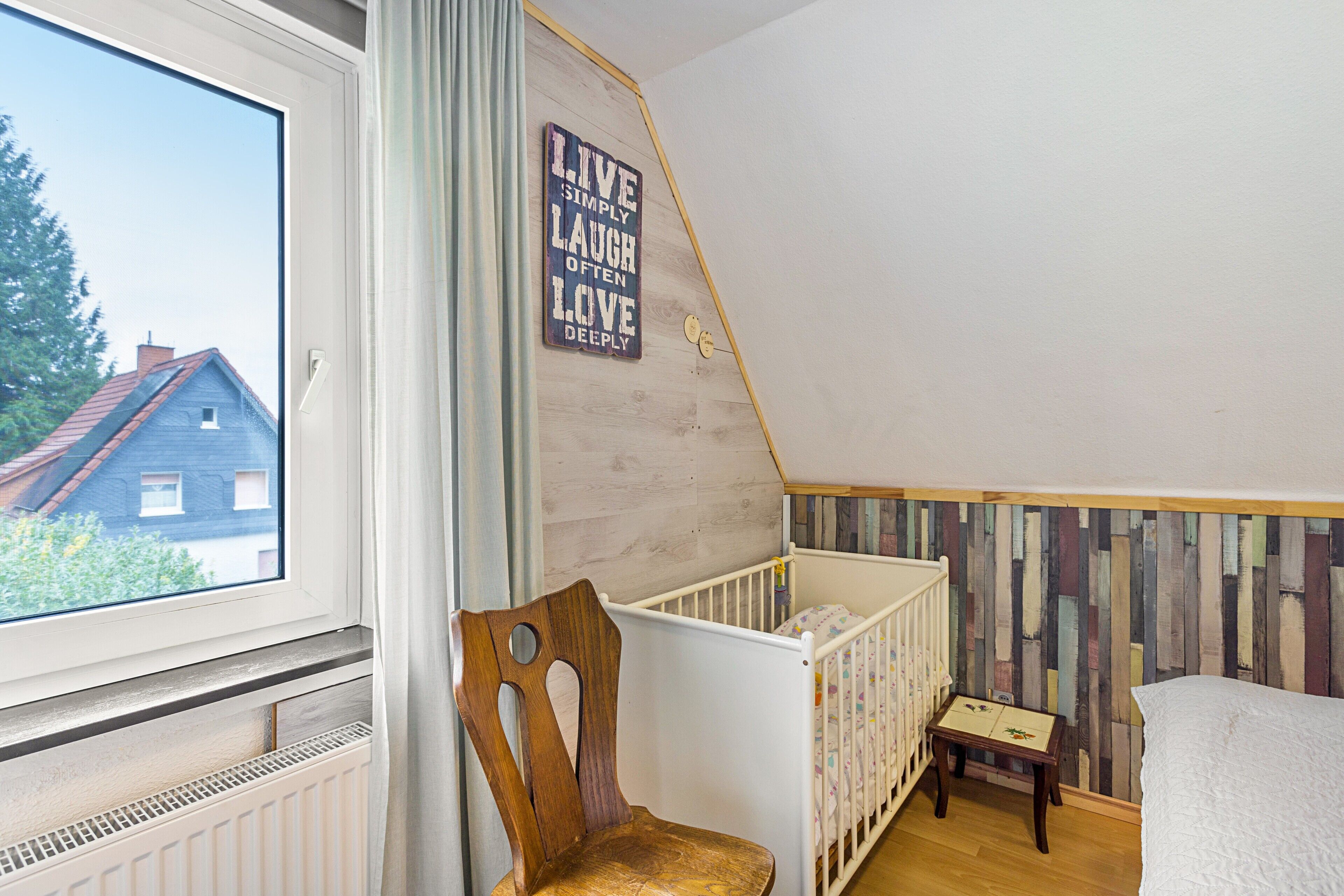 A room with a crib, a wooden chair, a small table, and a wall with a motivational quote.