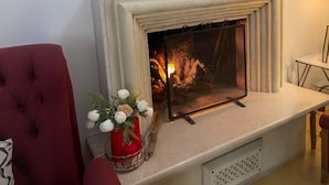 A living room with a fireplace, a red armchair, and two framed pictures on the wall.