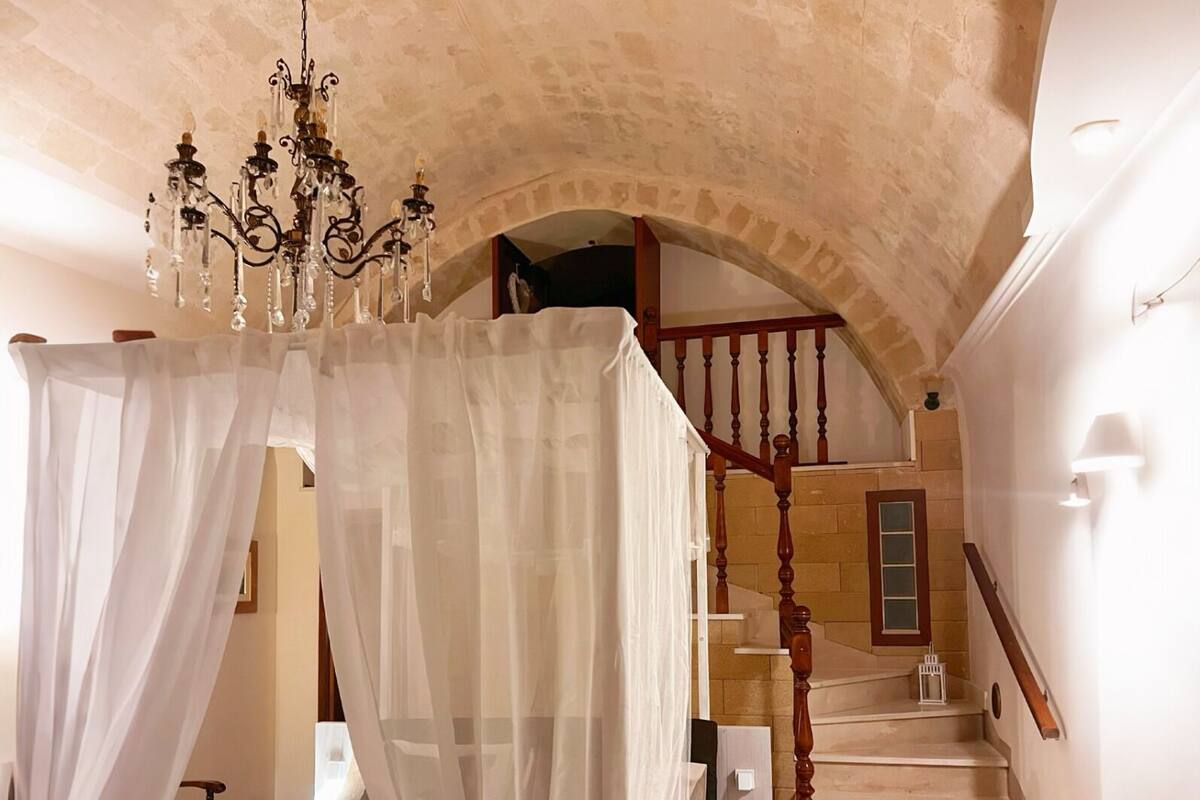 A bedroom with a four-poster bed, a chandelier, and a staircase leading to an upper level.