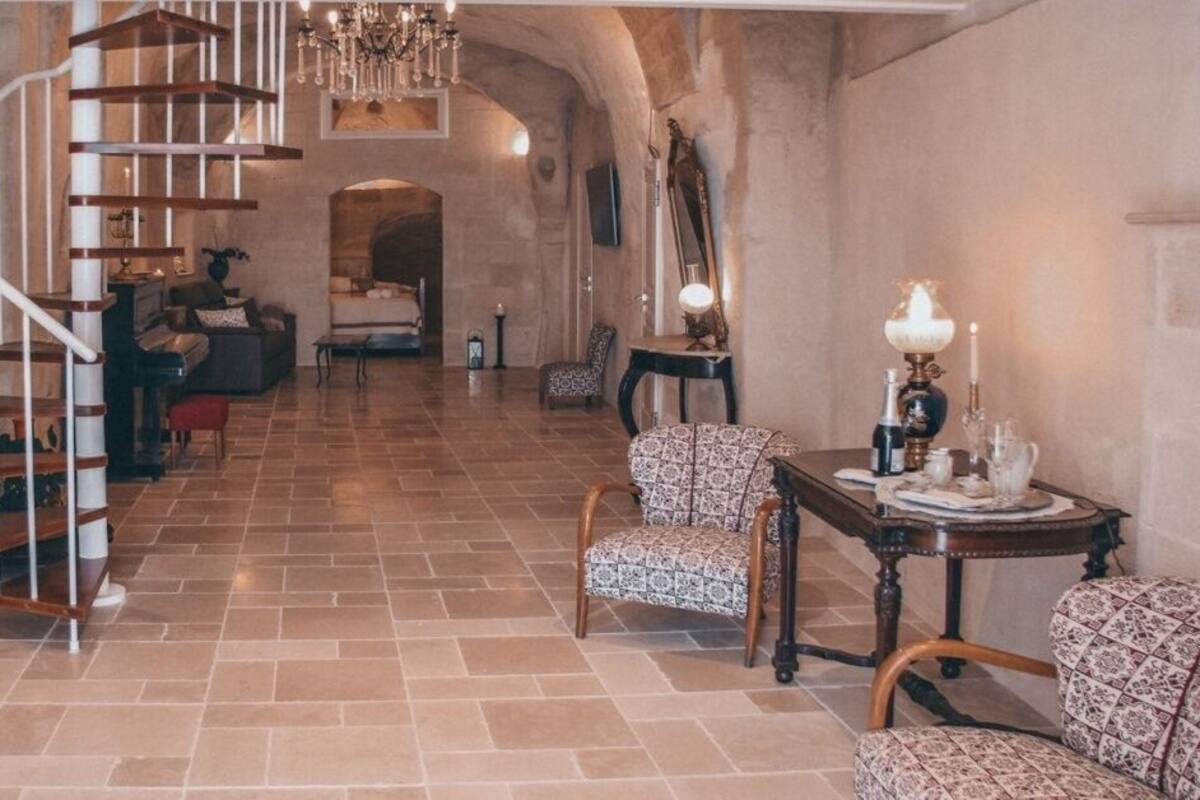 A spacious living area with a wooden staircase, a chandelier, and a cozy seating arrangement.