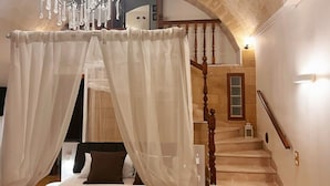 A bedroom with a four-poster bed, a chandelier, and a staircase.