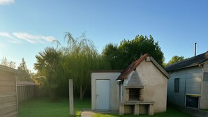 A backyard with a stone pathway leading to a barbecue area, a shed, and a small house. - Pleasant single-storey house in a quiet neighbourhood (Vierzon)
