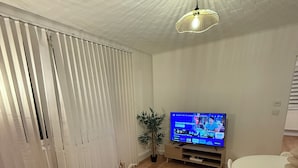 A modern living room with a black sofa, a round coffee table, a white dining table, and a TV on a wooden stand. - Pleasant single-storey house in a quiet neighbourhood (Vierzon)