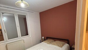 A bedroom with a bed, a window, a radiator, a nightstand, and a lamp. - Pleasant single-storey house in a quiet neighbourhood (Vierzon)