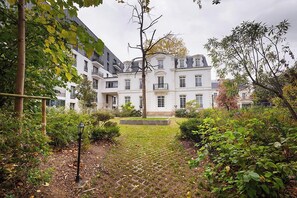 A courtyard with a paved pathway leading to a building with multiple windows and a central entrance. - Zenao Appart'hôtels Saint-Mandé (Saint-Mandé)