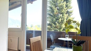 Una habitación con un ventanal grande, una mesa con una silla, una planta en maceta y un radiador.