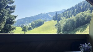 Una habitación con vistas a un paisaje verde, una pequeña mesa con una planta y un banco de madera.