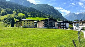 Un pueblo rural de montaña con edificios de varios pisos, un campo verde y montañas al fondo.