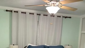 A bedroom with a bed, two bedside lamps, a ceiling fan, and a window with curtains.