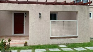 A two-story building with a red door, a small porch, and a white fence.